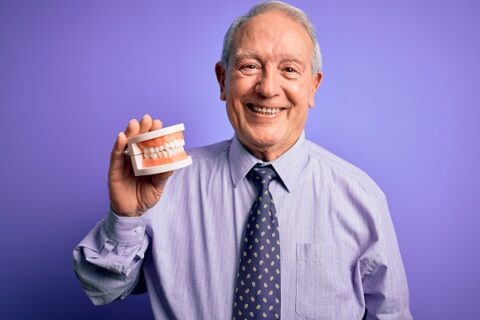 Smiling man holding dental model, purple background.