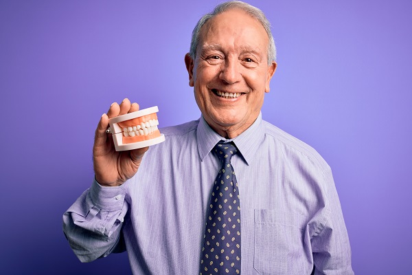 Smiling man holding dental model, purple background.