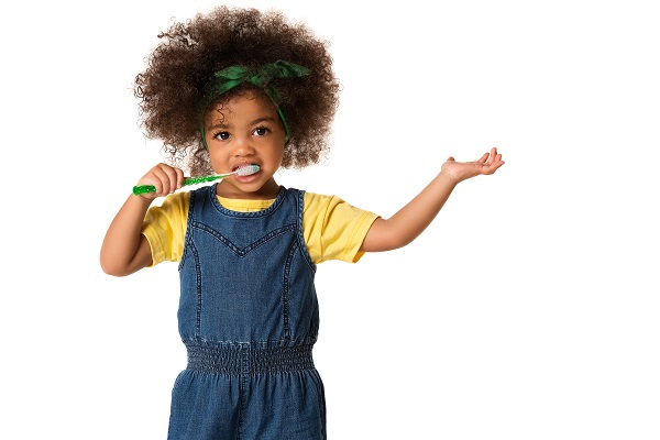 Child brushing teeth, wearing denim outfit.