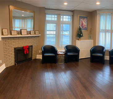 A cozy living room with three black chairs and a white brick fireplace.