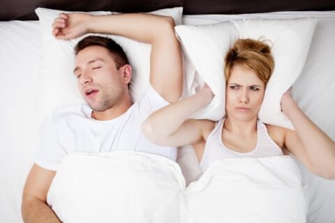 Man snoring, woman covering ears in bed.