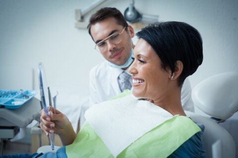 Patient smiling while holding dental mirror.